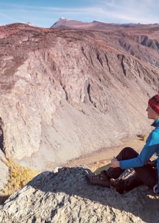 Hiker with backpack standing on top of a mountain with raised hands and enjoying sunrise