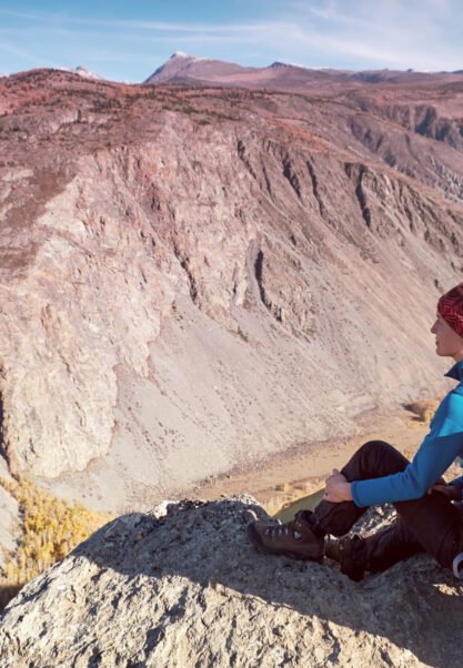 Hiker with backpack standing on top of a mountain with raised hands and enjoying sunrise