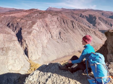 Hiker with backpack standing on top of a mountain with raised hands and enjoying sunrise
