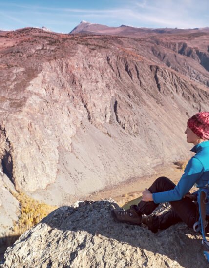 Hiker with backpack standing on top of a mountain with raised hands and enjoying sunrise