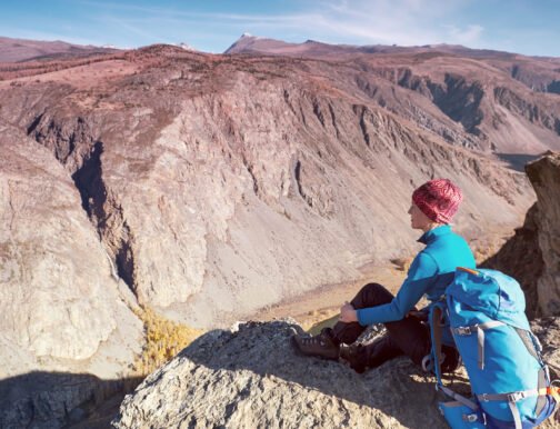 Hiker with backpack standing on top of a mountain with raised hands and enjoying sunrise