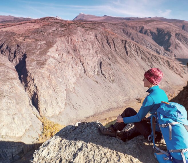 Hiker with backpack standing on top of a mountain with raised hands and enjoying sunrise
