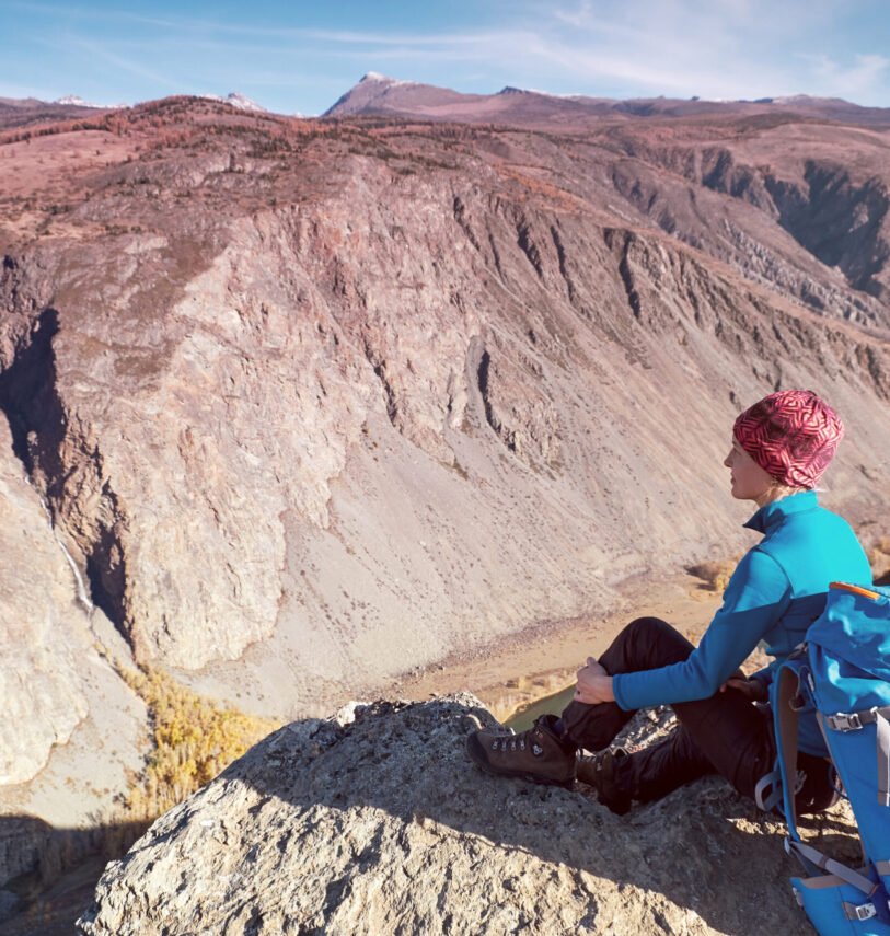 Hiker with backpack standing on top of a mountain with raised hands and enjoying sunrise
